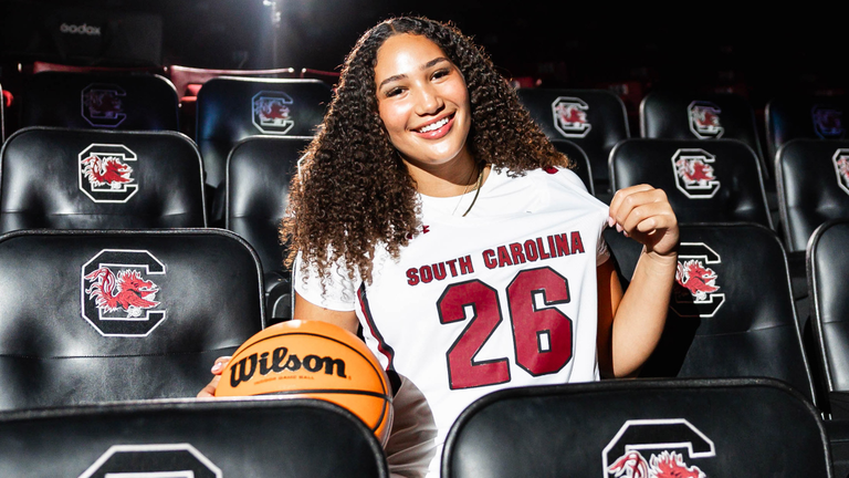 Kaeli Wynn in white uniform in black arena seating.