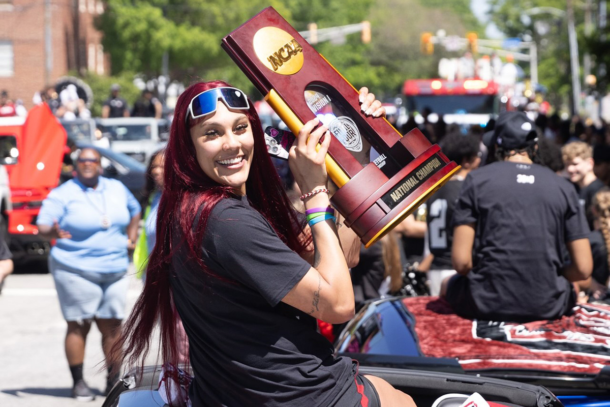 Kamilla Cardoso looks to camera with the National Championship trophy in the parade