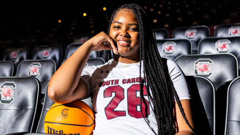 Kelsi Andrews in white uniform in black arena seating.