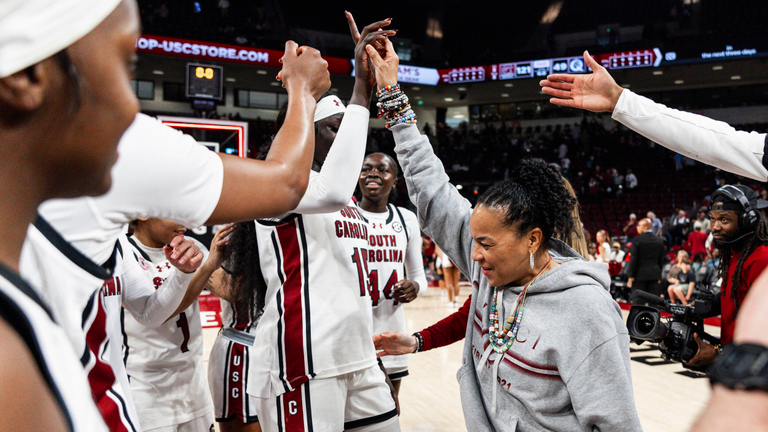 Dawn Staley reaches up as players begin to form a huddle around her.