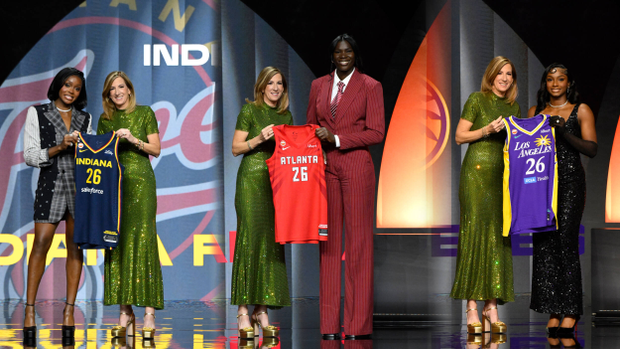 Raven Johnson, Madina Okot, Ta'Niya Latson on stage with WNBA Commissioner Cathy Engelbert holding up their team jerseys.