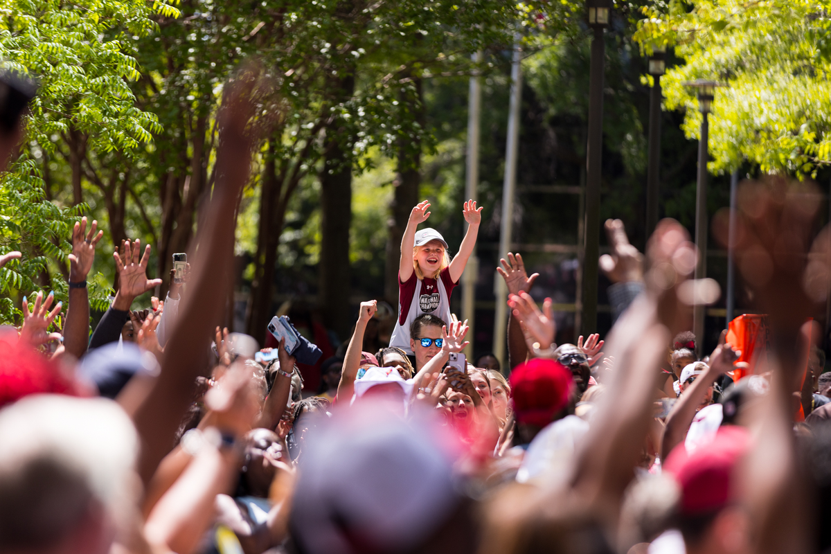 A young fan on shoulders reaches up with the crowd toward the team riding by in the National Championship parade.