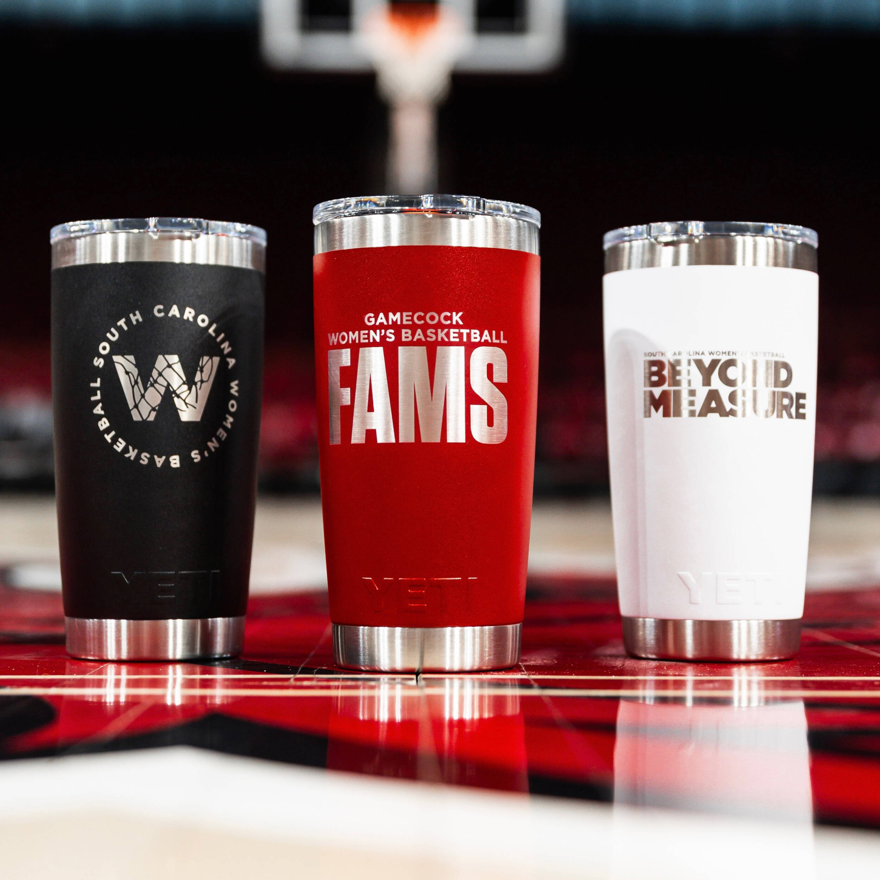 Three women's basketball YETI Ramblr tumblers on the court, left to right black, garnet and white.