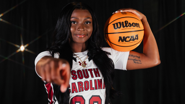 Ta'Niya Latson points at the camera in a studio photo on black background with star lights behind her.