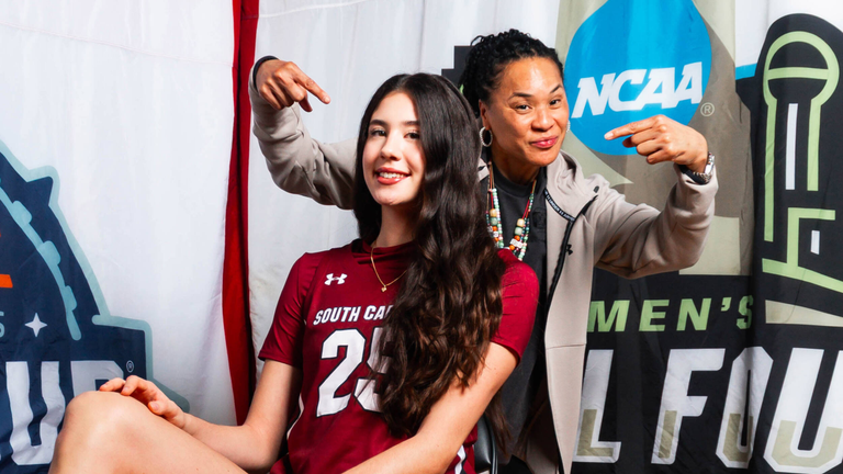 Alicia Tournebize seated wearing a garnet uniform with Dawn Staley standing behind pointing at her.